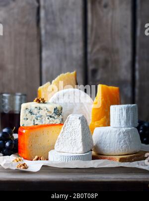 Assortiment de fromages : fromage bleu, fromage à pâte dure, fromage à pâte molle sur papier parchemin. Fond en bois. Espace de copie. Banque D'Images