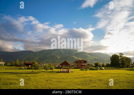 Champ d'herbe verte avec chalet touristique, belvédères, trottoir en bois, tentes touristiques, et montagnes cultivées de forêt sur l'arrière-plan et ciel nuageux Banque D'Images