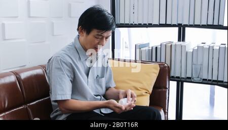 Homme asiatique senior prenant des médicaments sur un canapé à la maison Banque D'Images