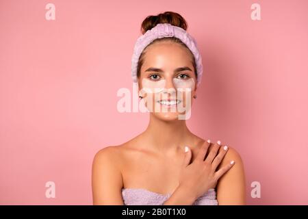 Une fille avec un bandage sur la tête et des correctifs sous ses yeux se dresse sur un fond rose avec sa main sur son épaule Banque D'Images