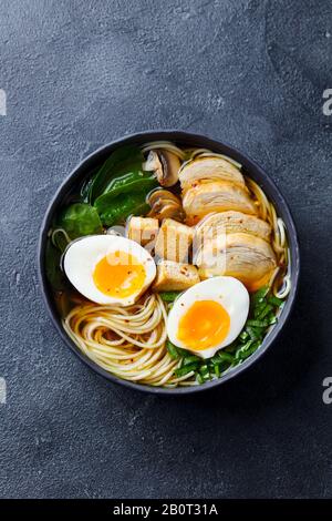 Soupe de nouilles asiatiques, ramen avec poulet, tofu, légumes et œufs dans un bol noir. Fond ardoise. Vue de dessus. Banque D'Images