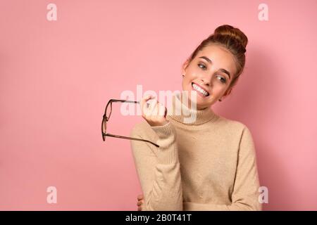 Une fille avec une peau propre et un haut support de pain et sourires artificiellement, regardant sur le côté et tient des verres par l'oreille. Banque D'Images