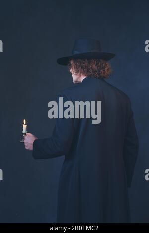 Homme mystérieux en manteau noir et chapeau tenant chandelier. Vue arrière. Banque D'Images