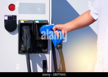 Station de charge électrique. La main du conducteur tient le chargeur pour les voitures électriques sur le parking de la ville. Concept de transport écologique. Alternative moderne ene Banque D'Images