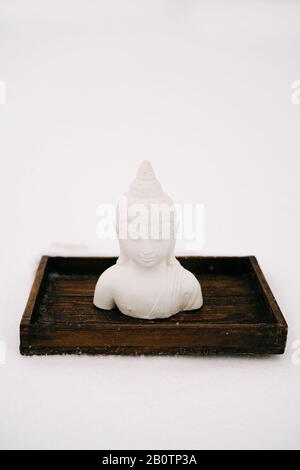 Figurine blanche de Bouddha faite de plâtre sur un support en bois pendant une chute de neige Banque D'Images