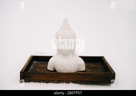 Figurine blanche de Bouddha faite de plâtre sur un support en bois pendant une chute de neige Banque D'Images