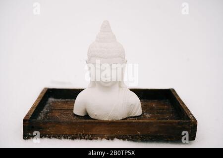 Figurine blanche de Bouddha faite de plâtre sur un support en bois pendant une chute de neige Banque D'Images