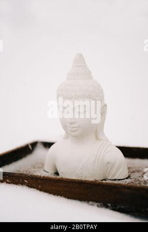 Figurine blanche de Bouddha faite de plâtre sur un support en bois pendant une chute de neige Banque D'Images