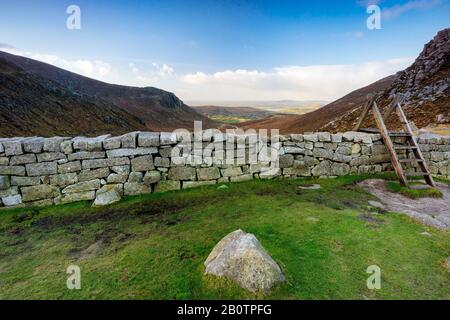 Mur de deuil avec échelle sur le Fossé De Lièvres supervisant la belle vallée avec le ciel bleu et les nuages blancs. La chaîne des montagnes Mourne en Irlande du Nord Banque D'Images