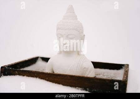 Figurine blanche de Bouddha faite de plâtre sur un support en bois pendant une chute de neige Banque D'Images