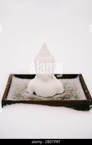 Figurine blanche de Bouddha faite de plâtre sur un support en bois pendant une chute de neige Banque D'Images