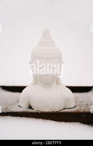 Figurine blanche de Bouddha faite de plâtre sur un support en bois pendant une chute de neige Banque D'Images