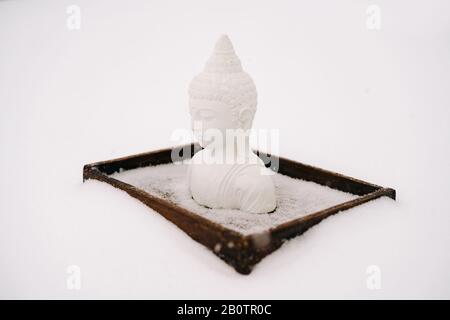 Figurine blanche de Bouddha faite de plâtre sur un support en bois pendant une chute de neige Banque D'Images