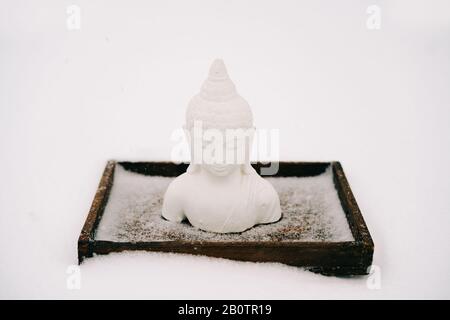 Figurine blanche de Bouddha faite de plâtre sur un support en bois pendant une chute de neige Banque D'Images