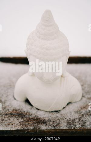 Figurine blanche de Bouddha faite de plâtre sur un support en bois pendant une chute de neige Banque D'Images