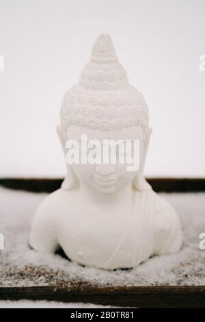 Figurine blanche de Bouddha faite de plâtre sur un support en bois pendant une chute de neige Banque D'Images