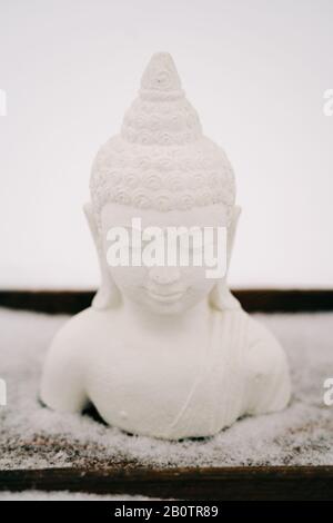 Figurine blanche de Bouddha faite de plâtre sur un support en bois pendant une chute de neige Banque D'Images