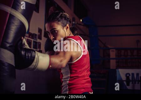 Boxer féminin portant un haut-training rouge dans la salle de sport, frappe sac de poinçon. Banque D'Images