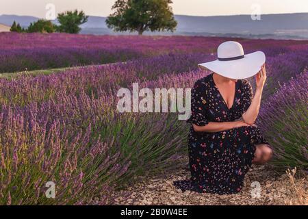 Fille dans une robe avec fleurs et grand chapeau blanc dans les champs de lavande en Provence, Valensole, France. Paysage pittoresque de la nature d'été et agracult Banque D'Images