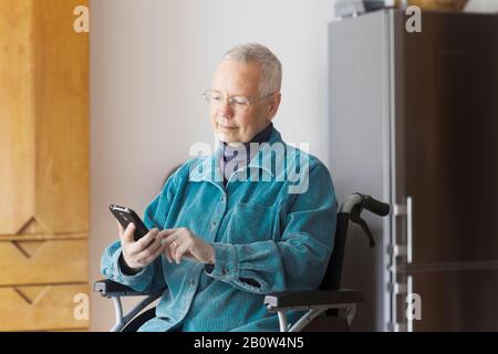 Femme âgée assise en fauteuil roulant, avec téléphone mobile. Banque D'Images