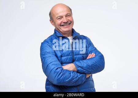 Homme senior en veste bleue avec bras croisés souriant isolé sur le mur blanc. Studio tourné Banque D'Images