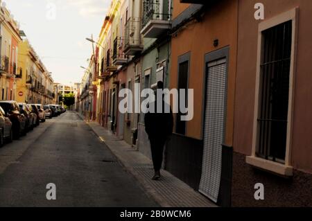 Figurine mâle corps entier, retour à l'appareil photo. Porter un chapeau, silhouette Imreconnaissable dans une ruelle espagnole avec une rangée de voitures sur la gauche et un peu d'oran Banque D'Images