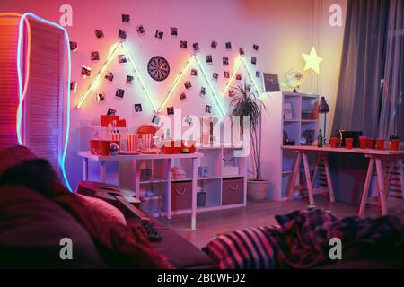 Image de la chambre domestique décorée avec des lumières et des verres vides pour les boissons et les bouteilles vides sur la table la fête est terminée Banque D'Images