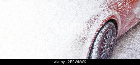 Voiture rouge lavée en auto-service carwash, détails sur le savon blanc pulvérisé sur la transition de surface au motif abstrait - large bannière avec de l'espace pour le texte laissé Banque D'Images