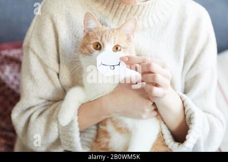 Gros plan sur le chat domestique mignon assis sur les genoux de la femme et la femme tenant du papier avec le sourire devant sa bouche Banque D'Images