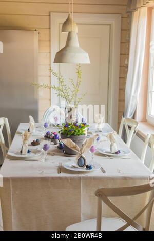 Décoration festive de table de Pâques, serviettes en forme d'oreilles de lapin, œufs de poule et de caille teints, gâteaux, violettes potées, plumes, dîner en famille o Banque D'Images