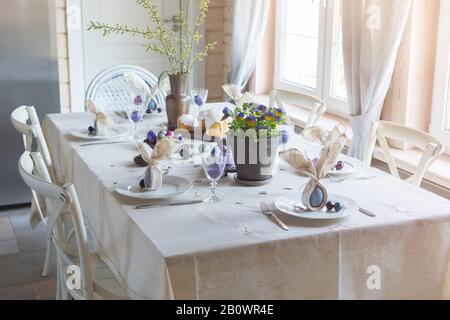 Décoration festive de table de Pâques, serviettes en forme d'oreilles de lapin, œufs de poule et de caille teints, gâteaux, violettes potées, plumes, dîner en famille o Banque D'Images