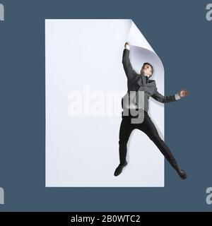 Imaginez qui couvre la feuille blanche pour obtenir l'icône de fichier numérique. Un jeune homme de style bureau qui attrape le bord d'une énorme feuille de papier. Monde numérique, imagination drôle de la façon dont l'icône apparaît. Banque D'Images