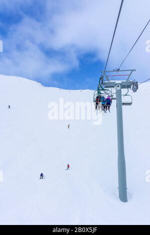 Les skieurs et planchistes non identifiables sur télésiège remontant une pente de ski dans la montagne enneigée (éventail des Rocheuses canadiennes. Banque D'Images