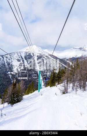 Les skieurs et planchistes non identifiables sur télésiège remontant une pente de ski dans la montagne enneigée (éventail des Rocheuses canadiennes. Banque D'Images