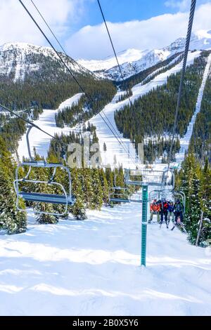 Les skieurs et planchistes non identifiables sur télésiège remontant une pente de ski dans la montagne enneigée (éventail des Rocheuses canadiennes. Banque D'Images