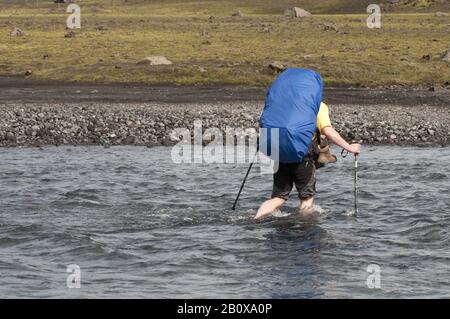 Le randonneur traverse une rivière sur le chemin de Skogar à Landmannalaugar, Islande, Europe, Banque D'Images