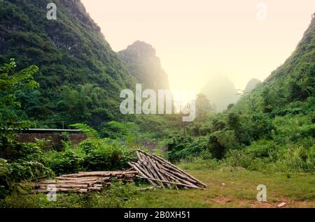 Vue sur le soleil levant derrière les montagnes karstiques de Guilin, Chine. Avec des forêts de bambou et une pile de bâtons de bambou au premier plan. Banque D'Images