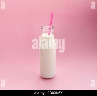 Bouteille de lait en verre avec une paille rose sur fond rose. Placer pour le texte. Pose plate. Vue de dessus. Banque D'Images