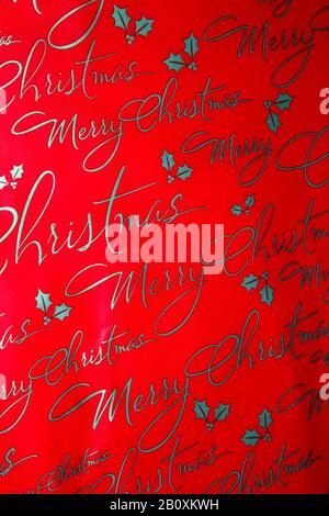 Détail du papier d'emballage avec un thème joyeux Noël et imprimé « joyeux Noël » dans un texte de script avec petites décorations holly Banque D'Images