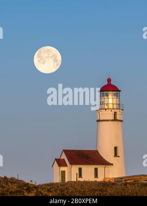 Phare du Cap Blanco au lever du soleil avec une « Lune de neige » comme ensemble pleine lune; parc national du Cap Blanco, côte sud de l'Oregon. (Photo composite de la lune an Banque D'Images