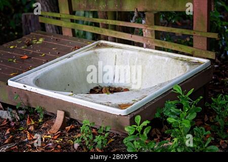 Une vieille baignoire a laissé abandonné et sale dans un jardin extérieur, entouré de mauvaises herbes Banque D'Images