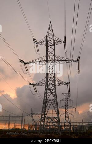 Silhouette de la tour de transmission et lignes de transmission haute tension, au coucher du soleil, avec ciel orange et nuages de tempête. Banque D'Images