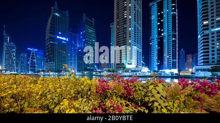 Gratte-ciel et zones vertes dans les tours des lacs de Jumeirah (JLT) la nuit, New Dubai, Emirats Arabes Unis, Banque D'Images