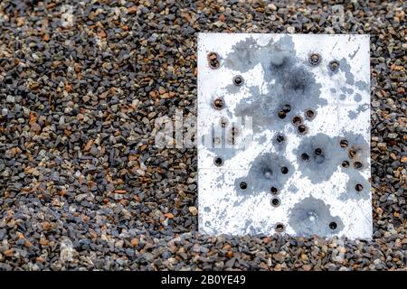 Un morceau de métal rempli de trous de balle. Le métal repose dans une pile de gravier humide sombre et semble être le dos d'un signe. Trous de puces. Banque D'Images