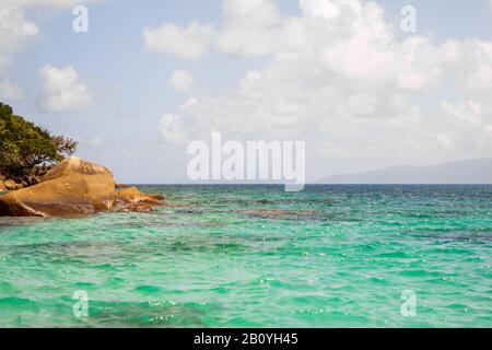 Nudey Beach, Fitzroy Island, les rochers traversent les eaux cristallines de la mer de corail avec la côte du Queensland Australie en arrière-plan. Banque D'Images