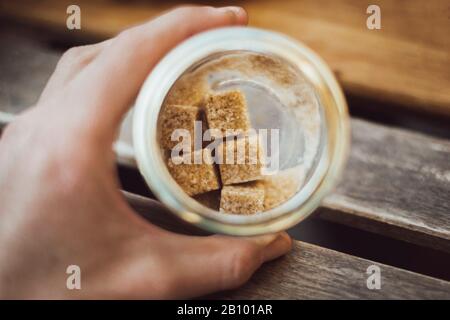 Verre avec des cubes de sucre brun à la main sur la table en bois Banque D'Images