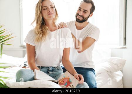 Un jeune couple heureux dans l'amour se détendre sur un canapé dans le salon, lire le magazine, rire, masser Banque D'Images