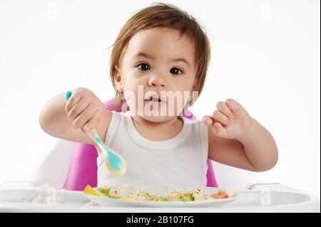 Joli bébé manger des aliments sains sur chaise haute isolé Banque D'Images