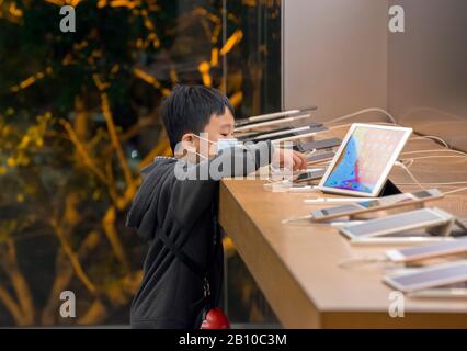 Jeune garçon chinois dans une boutique d'ordinateurs jouant avec des ordinateurs portables et des smartphones, Hong Kong, Chine. Banque D'Images