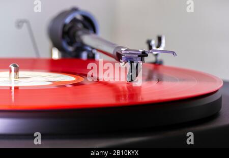 L'aiguille / le stylet sur les rainures d'un enregistrement vinyle LP rouge, sur un plateau tournant, jouant une piste d'album de musique. Banque D'Images